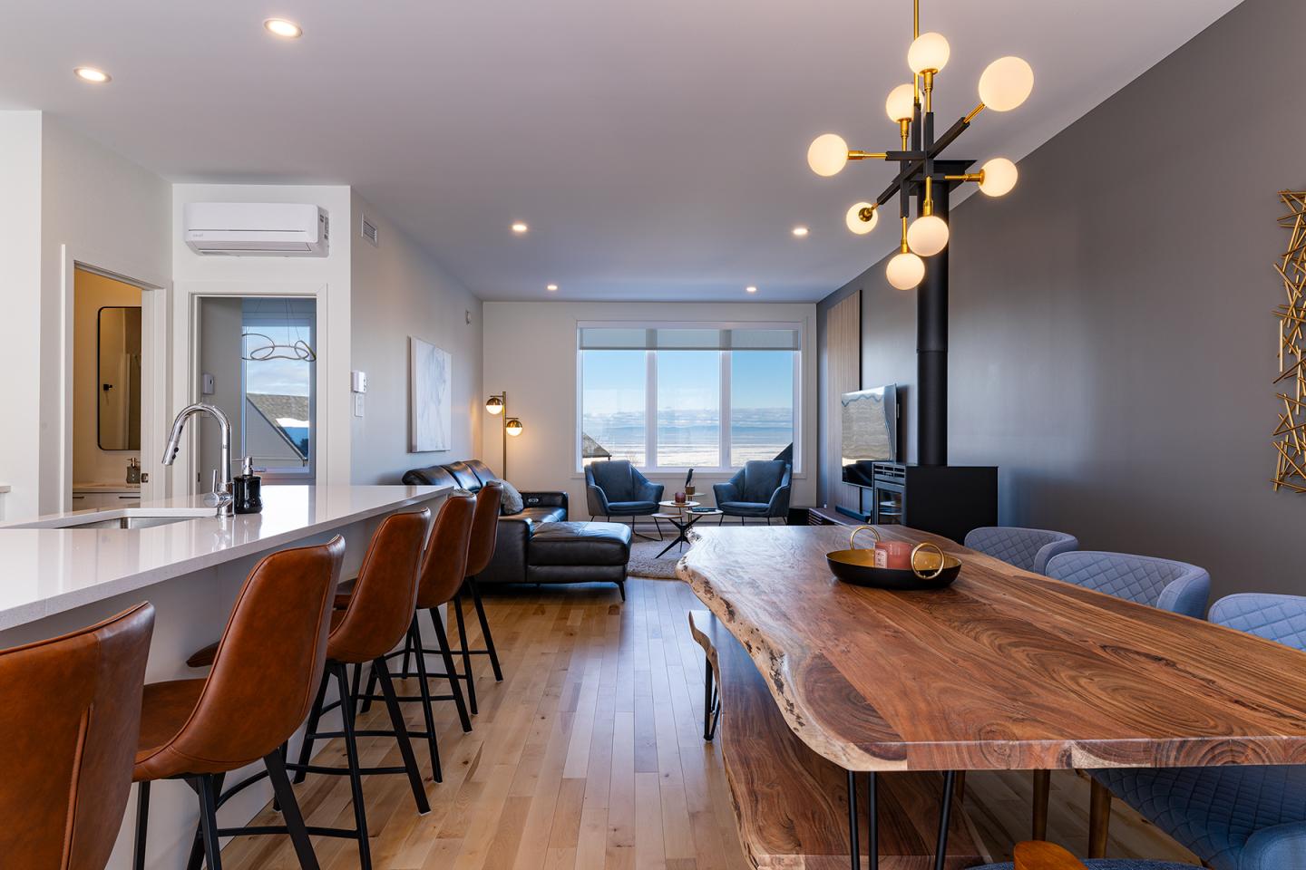 Salle à manger moderne avec table en bois massif, chaises en cuir, et grande fenêtre.