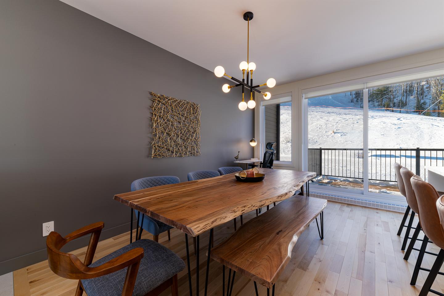 Salle à manger moderne avec grande table en bois, baies vitrées et lustre design.
