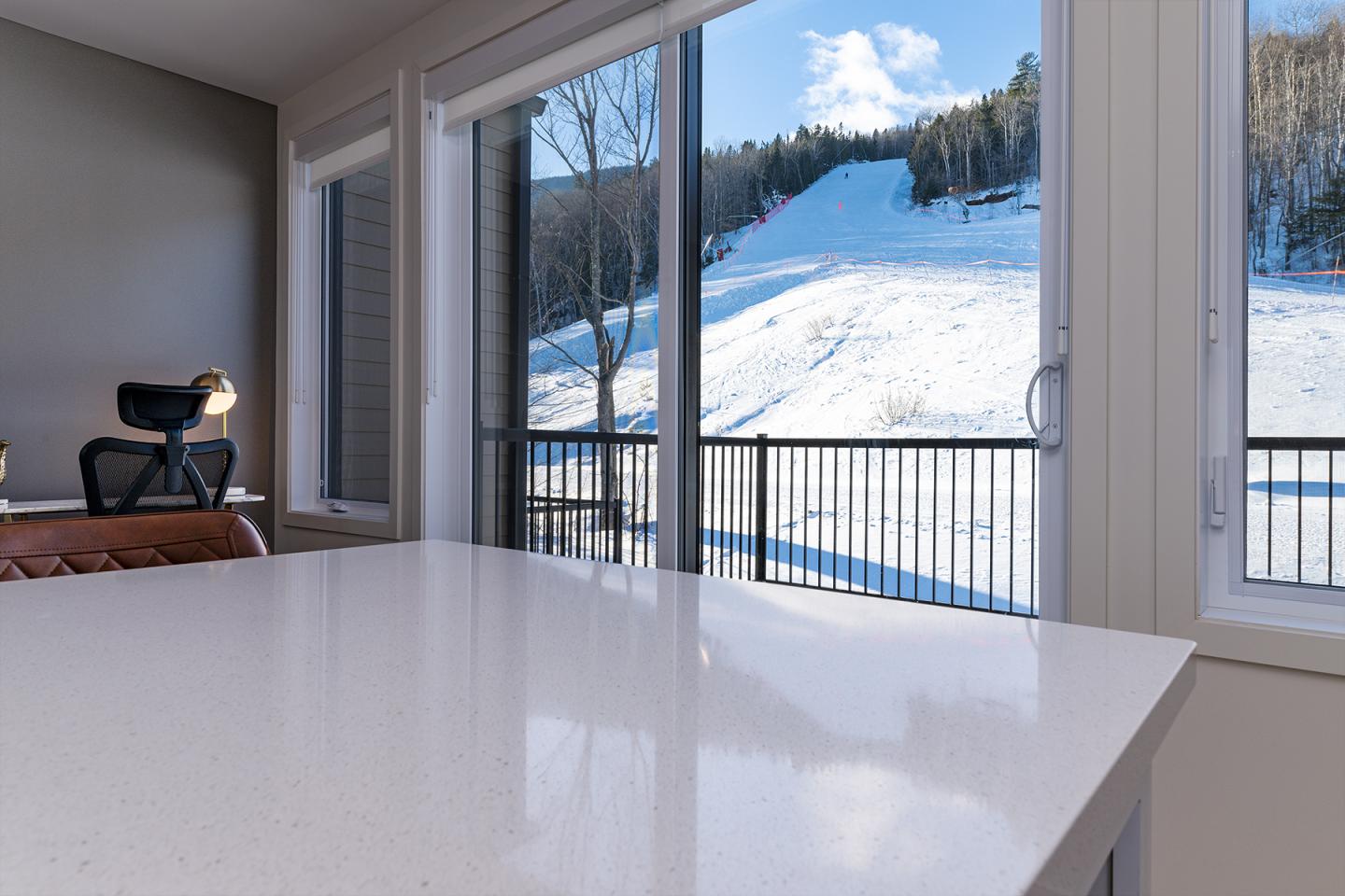 Vue sur piste enneigée depuis un intérieur moderne, grandes fenêtres, ambiance lumineuse.
