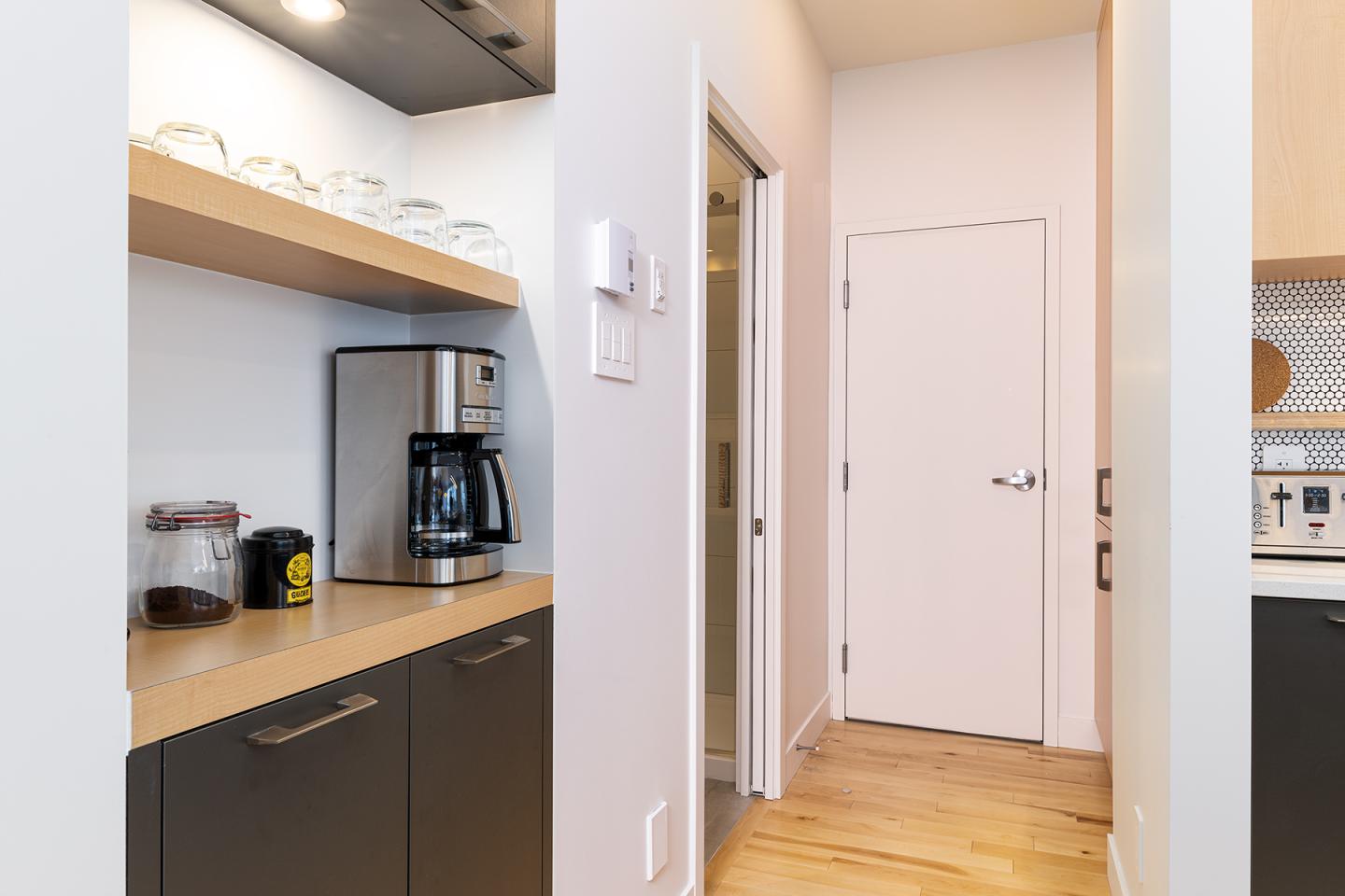 Cuisine moderne avec cafetière, placards noirs et sol en bois clair.