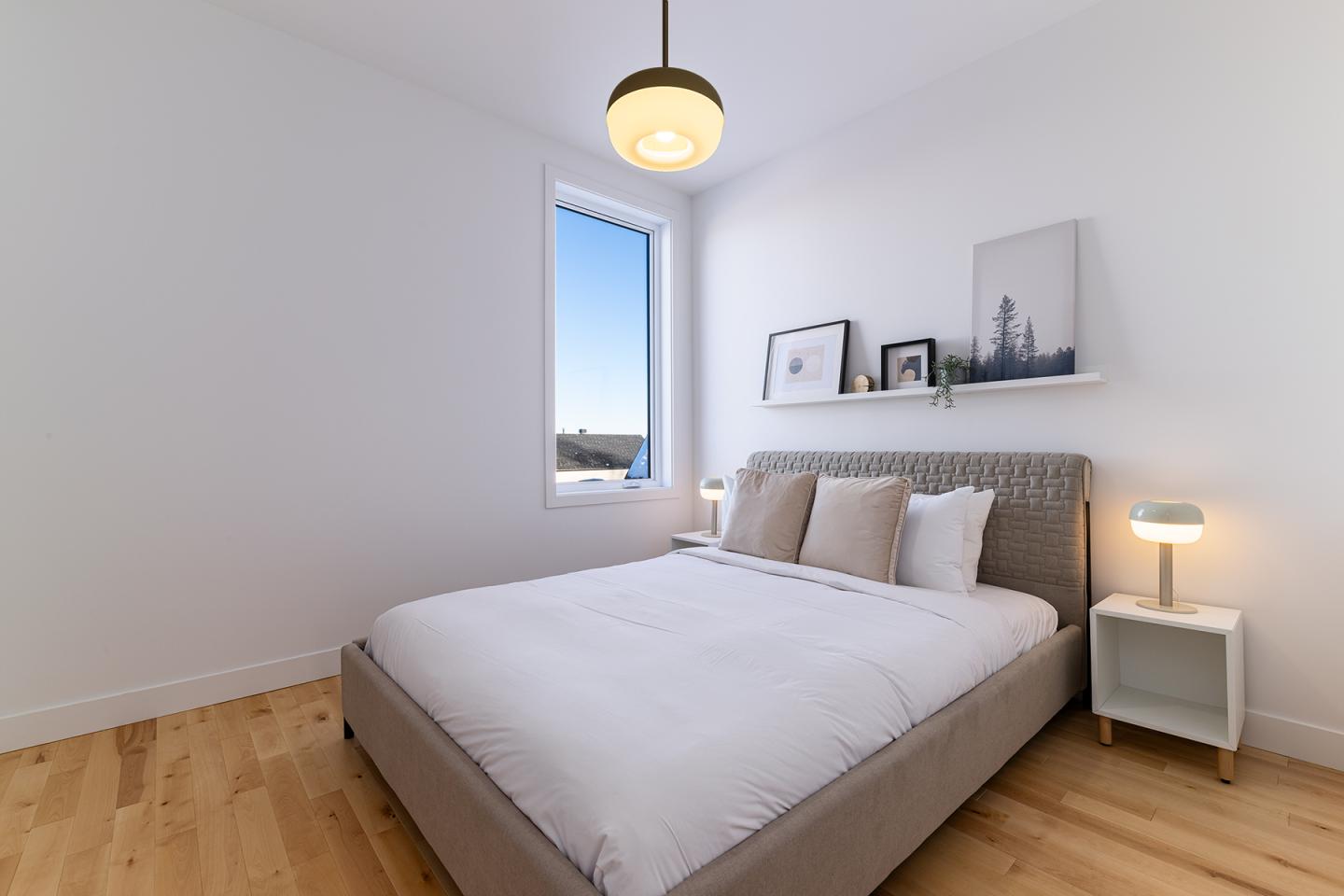 Chambre lumineuse avec lit double, lampe suspendue et fenêtre avec vue.