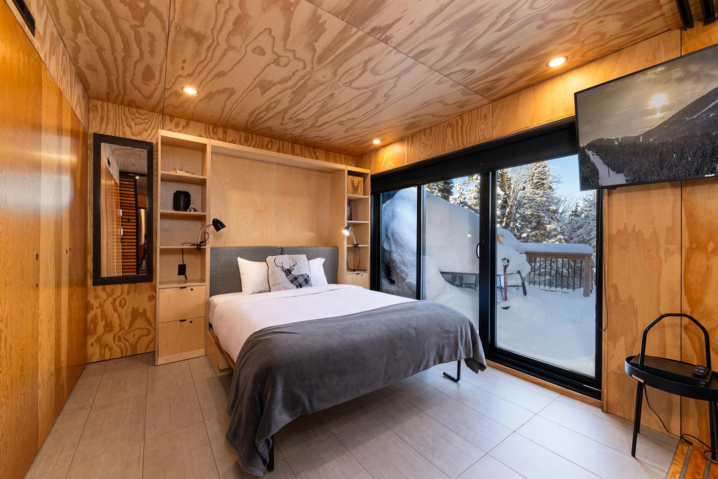 Chambre moderne en bois, lit double, grande baie vitrée avec vue sur la neige.