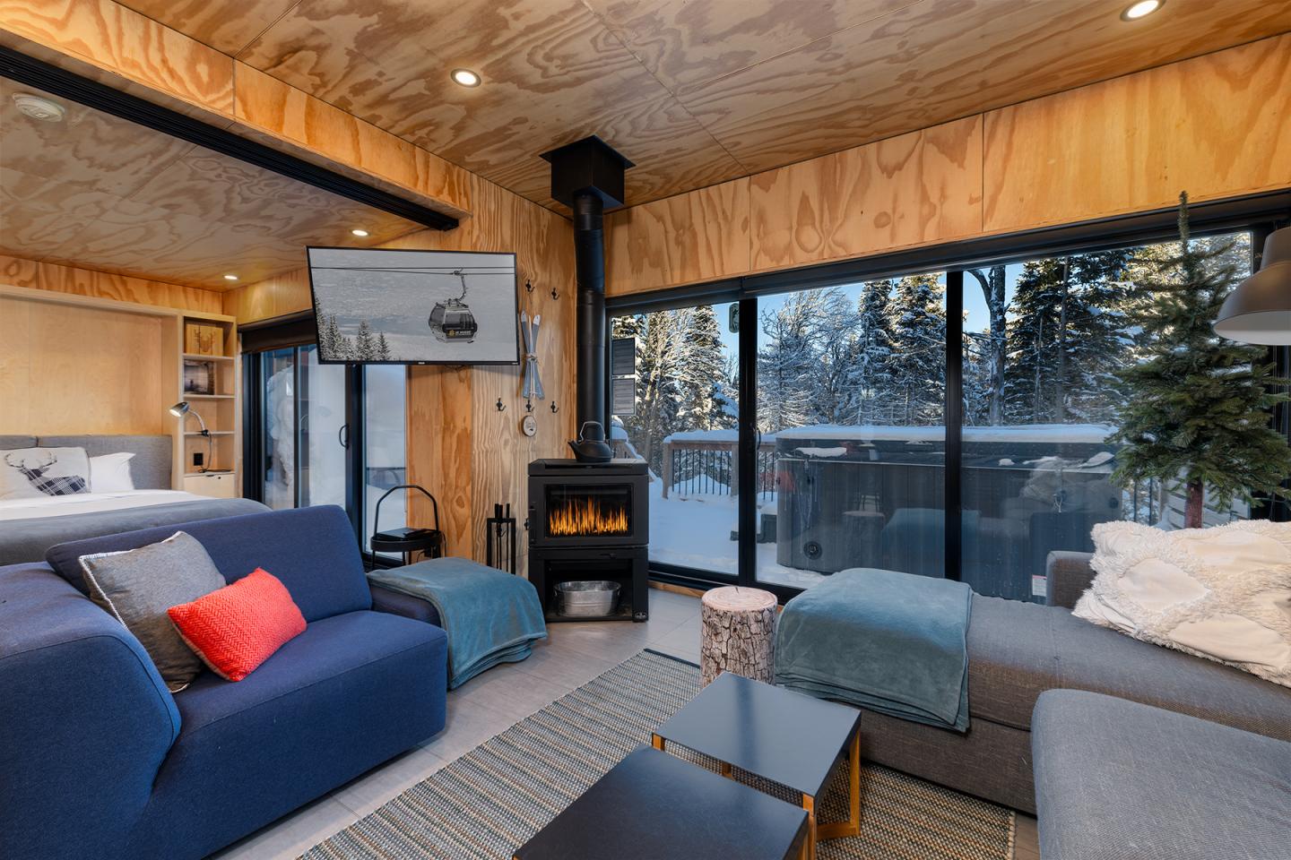Salon moderne avec poêle, canapé bleu, grandes fenêtres donnant sur la neige.