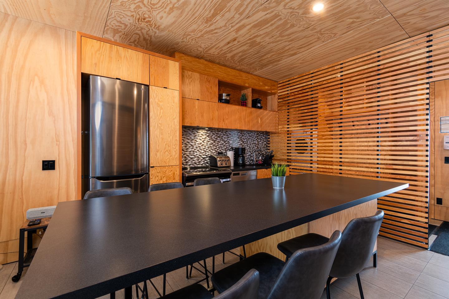 Cuisine moderne en bois, avec réfrigérateur en acier, table noire et chaises.