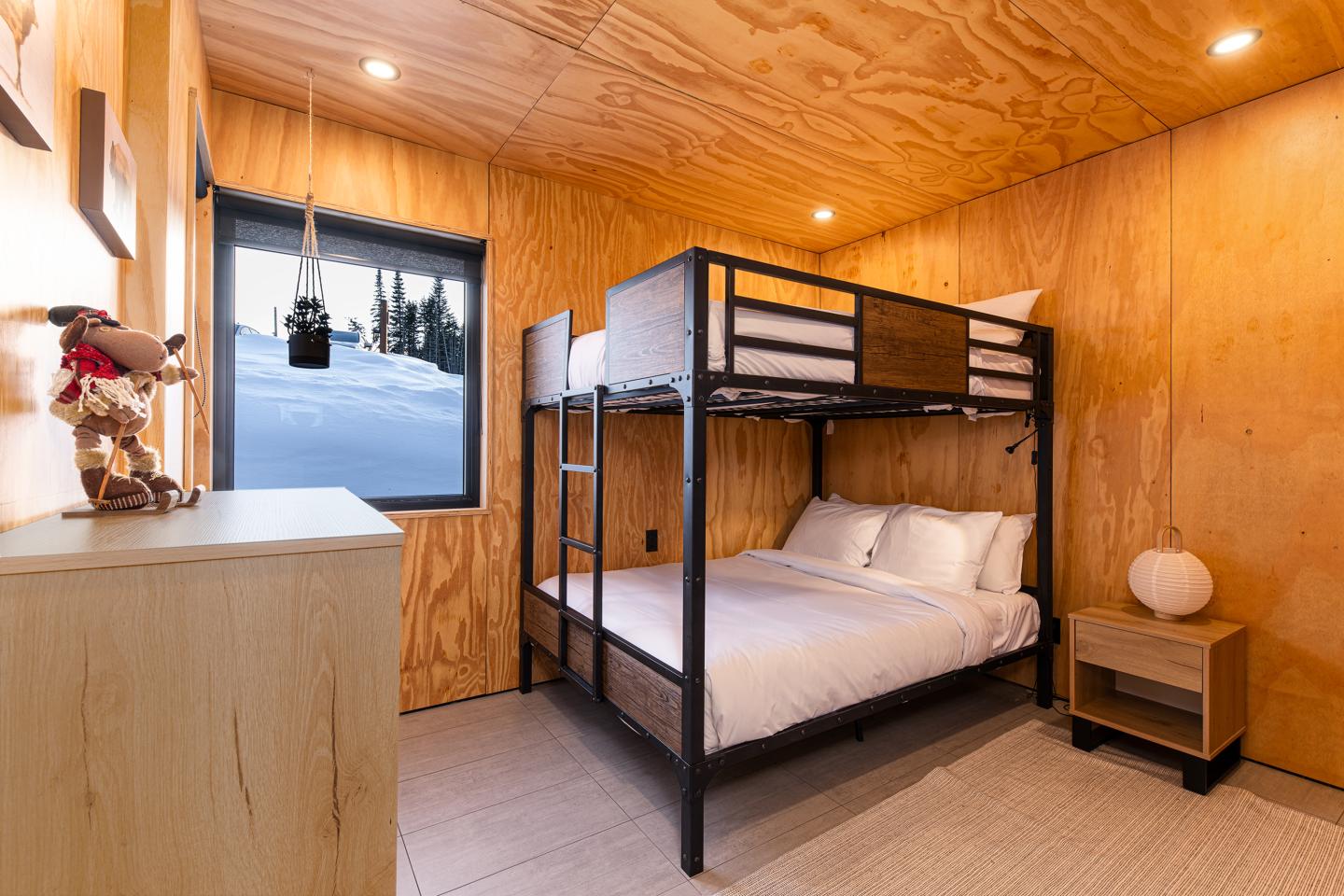 Chambre en bois avec un lit superposé et une grande fenêtre.