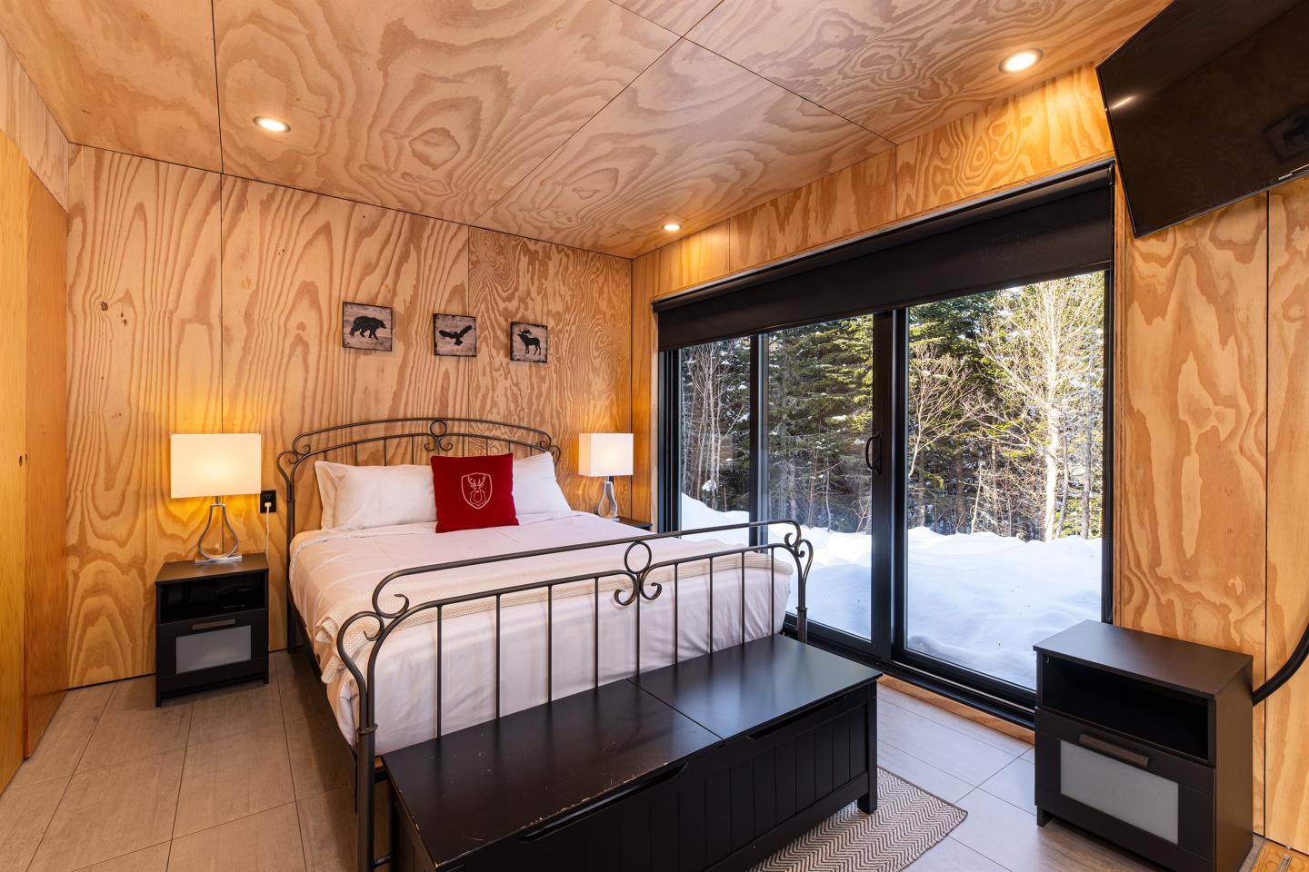 Chambre en bois clair avec lit double, vue sur la neige par une grande fenêtre.