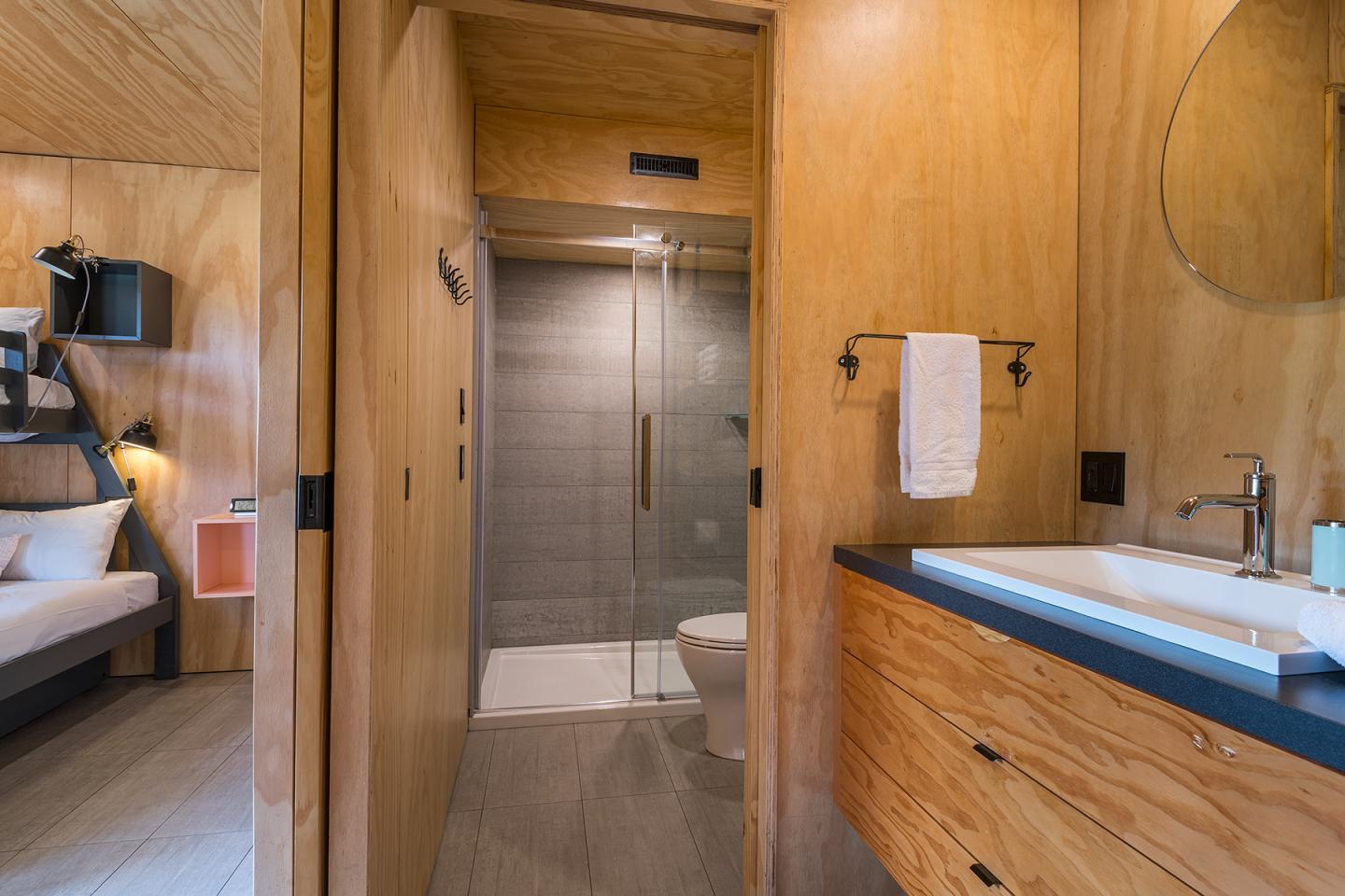 Salle de bain moderne en bois clair avec douche en verre et lavabo.
