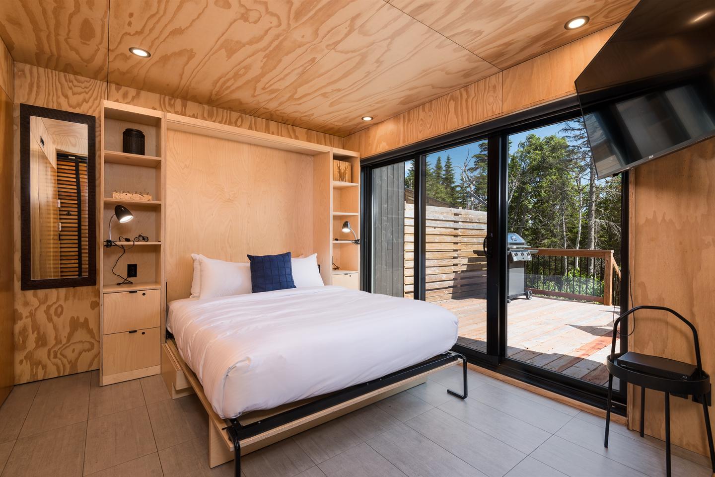 Chambre moderne avec lit double, grandes fenêtres et terrasse en bois.