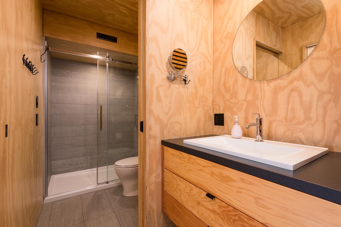 Salle de bain en bois clair avec douche vitrée et lavabo blanc.