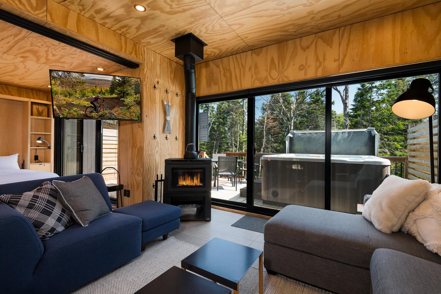 Salon moderne en bois, avec poêle, canapé bleu, jacuzzi extérieur.