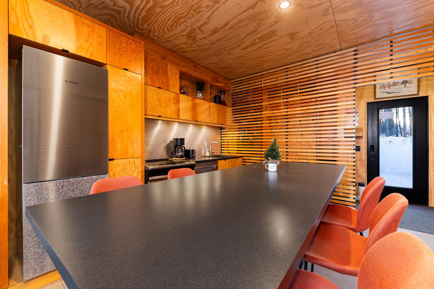 Cuisine moderne avec table noire, chaises rouges et bois clair.