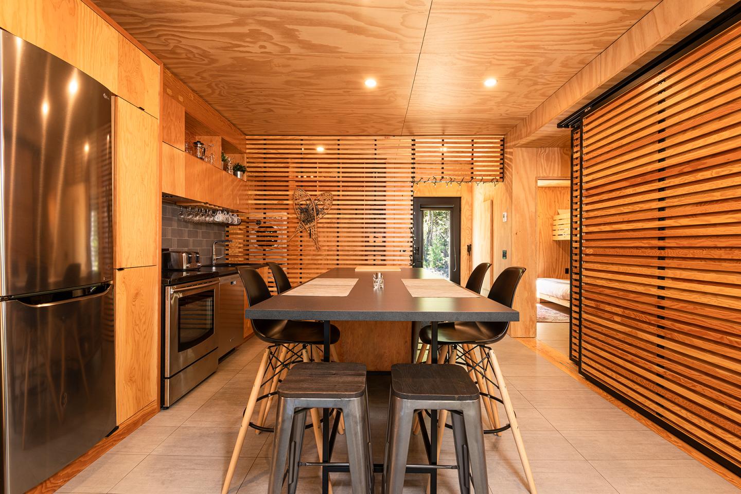 Cuisine moderne en bois avec îlot central, tabourets et électroménager en acier inoxydable.
