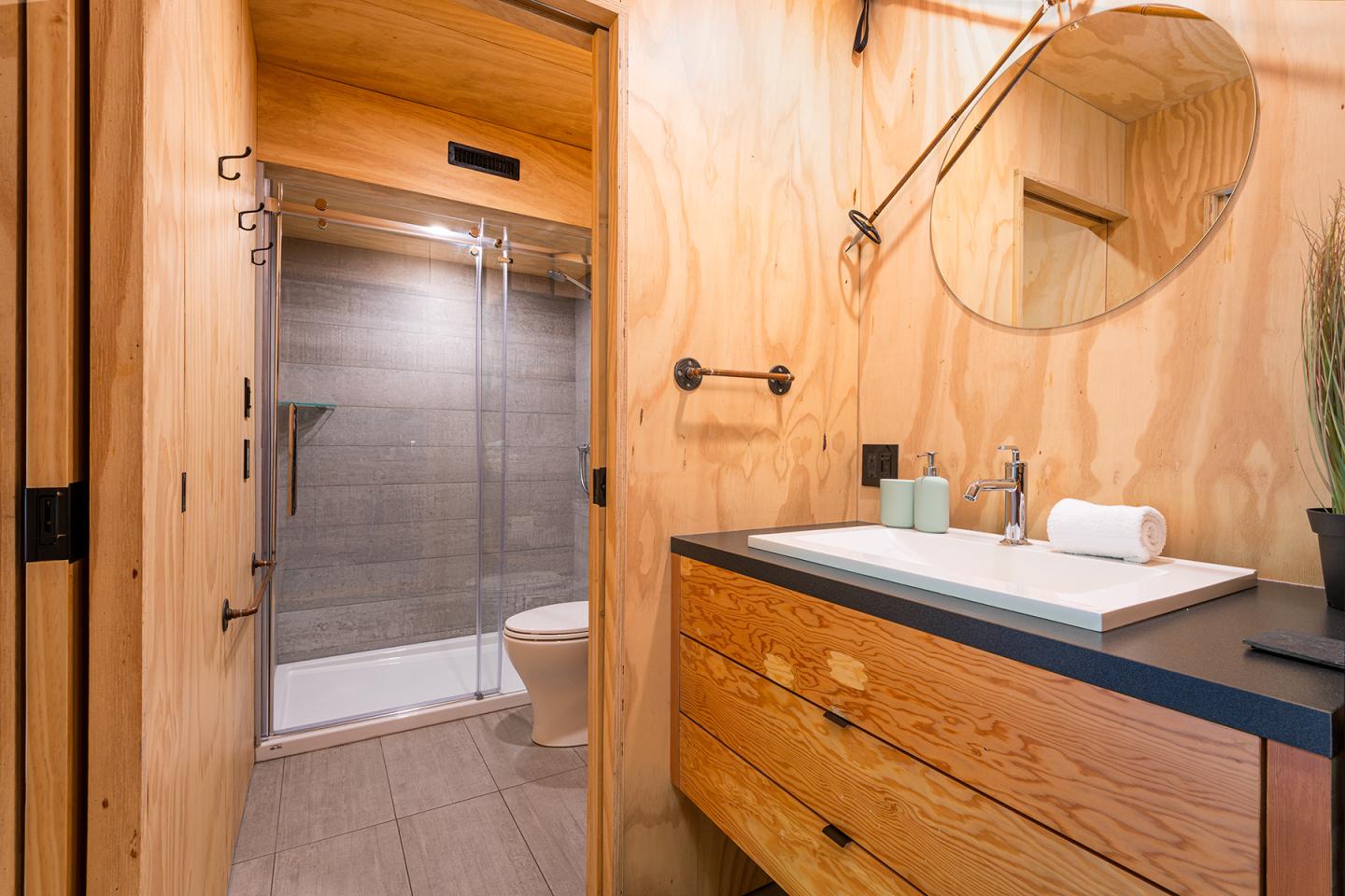 Salle de bain moderne en bois, lavabo et douche avec parois en verre.