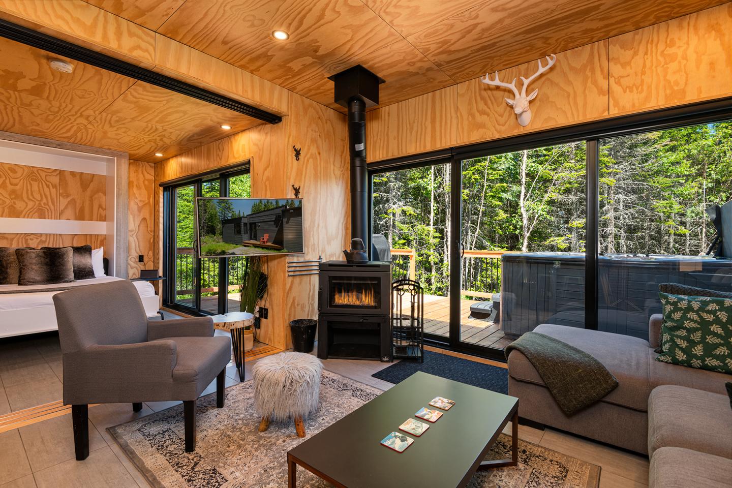 Salon confortable en bois avec cheminée, grandes fenêtres donnant sur la forêt.