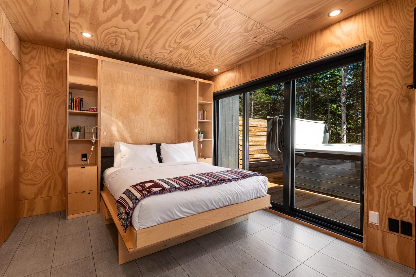 Chambre chaleureuse en bois, lit double, grande fenêtre donnant sur terrasse ensoleillée.