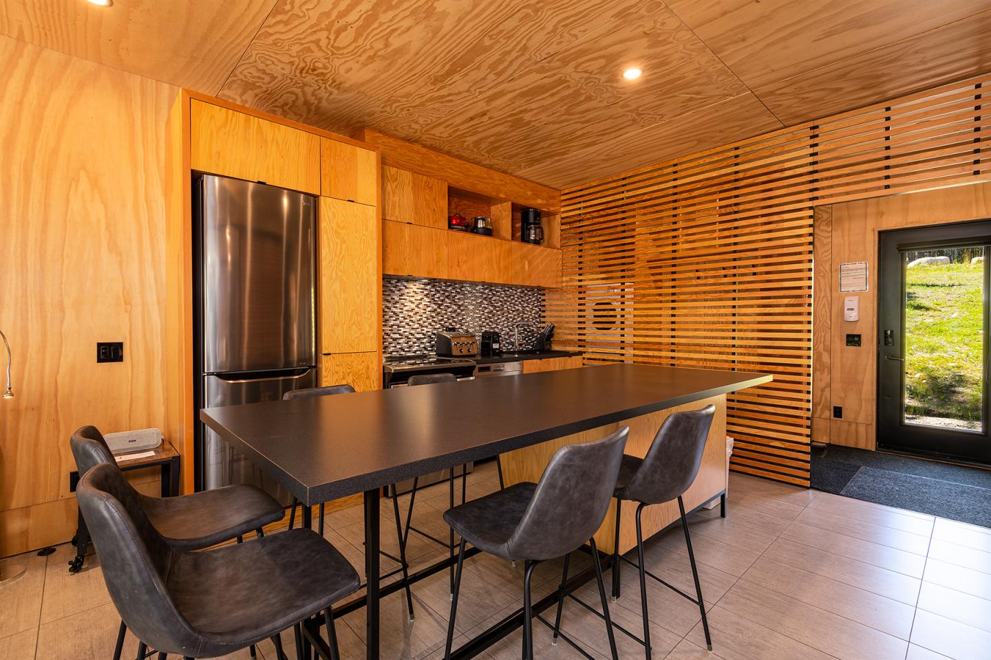 Cuisine moderne en bois avec table haute et tabourets, réfrigérateur en inox.