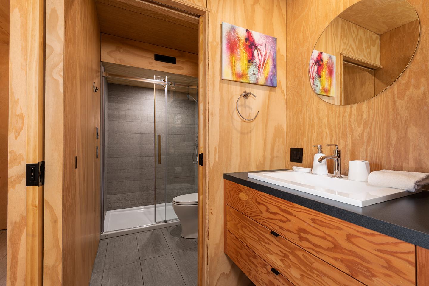 Salle de bain moderne en bois avec douche vitrée et lavabo double.