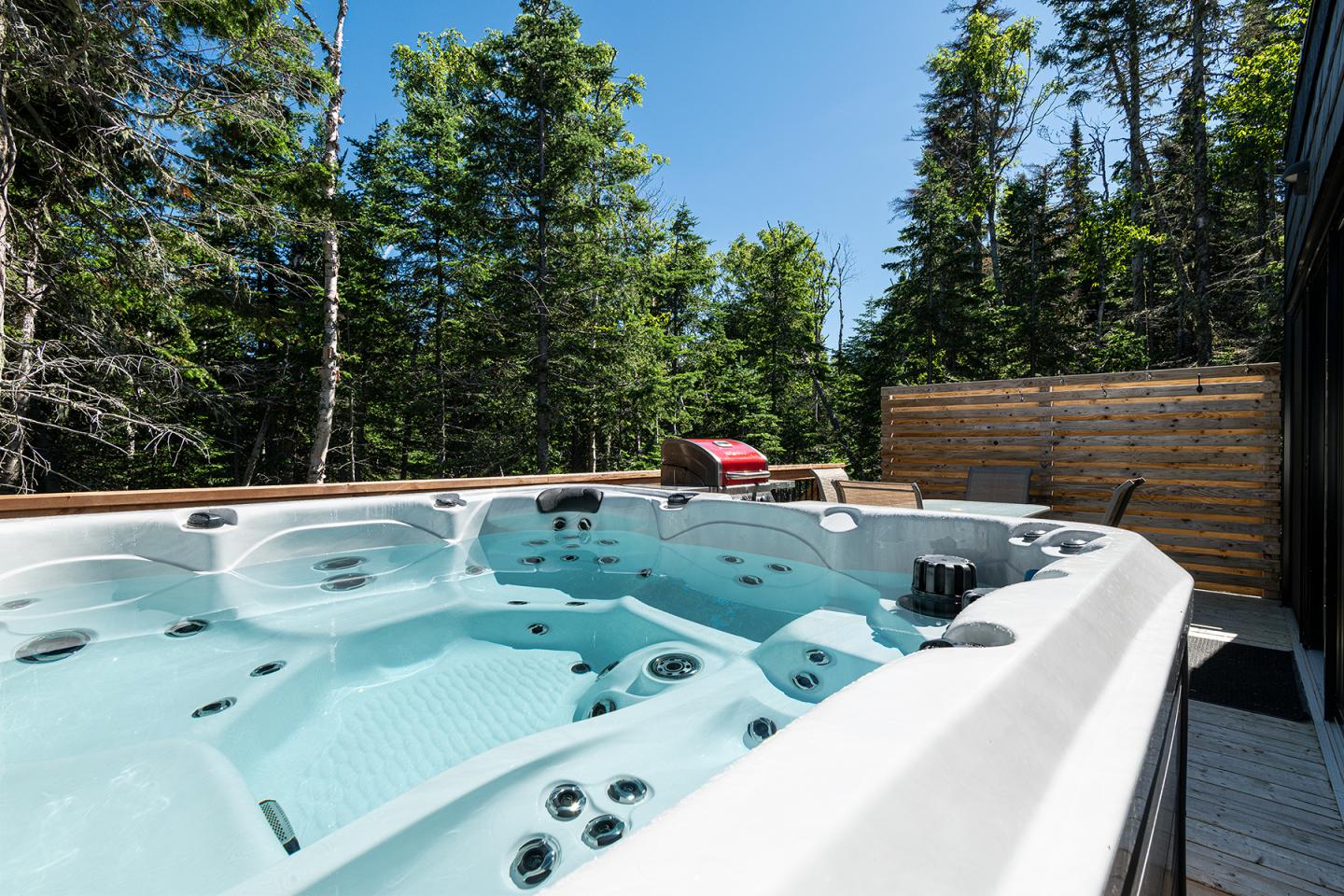 Spa extérieur entouré d'arbres, ciel bleu clair.