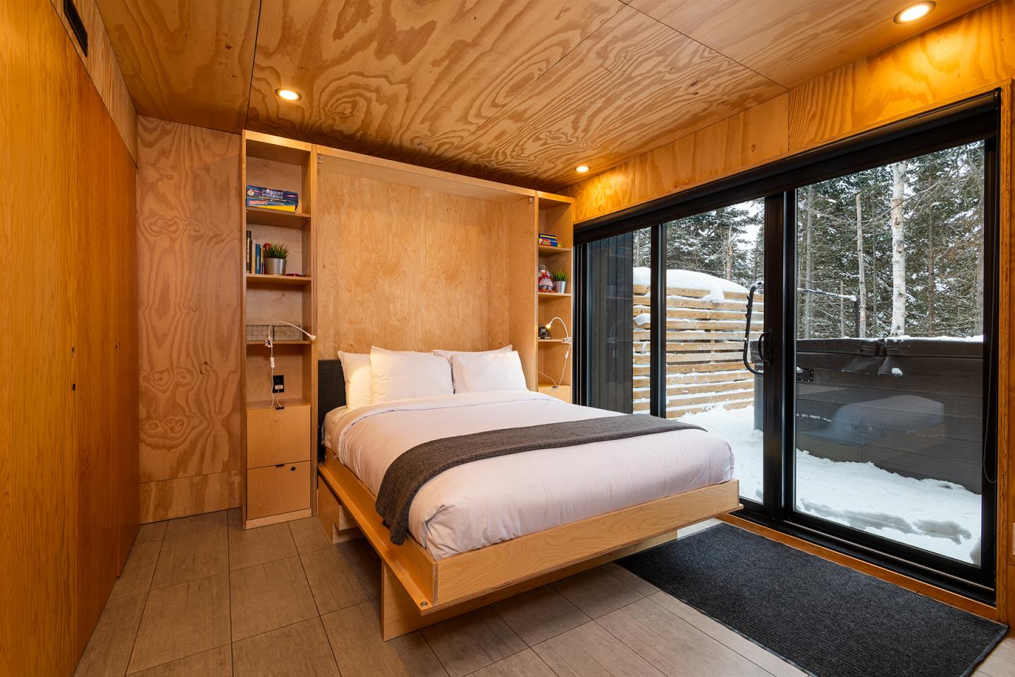 Chambre moderne en bois avec lit double, vue sur la neige à travers une baie vitrée.