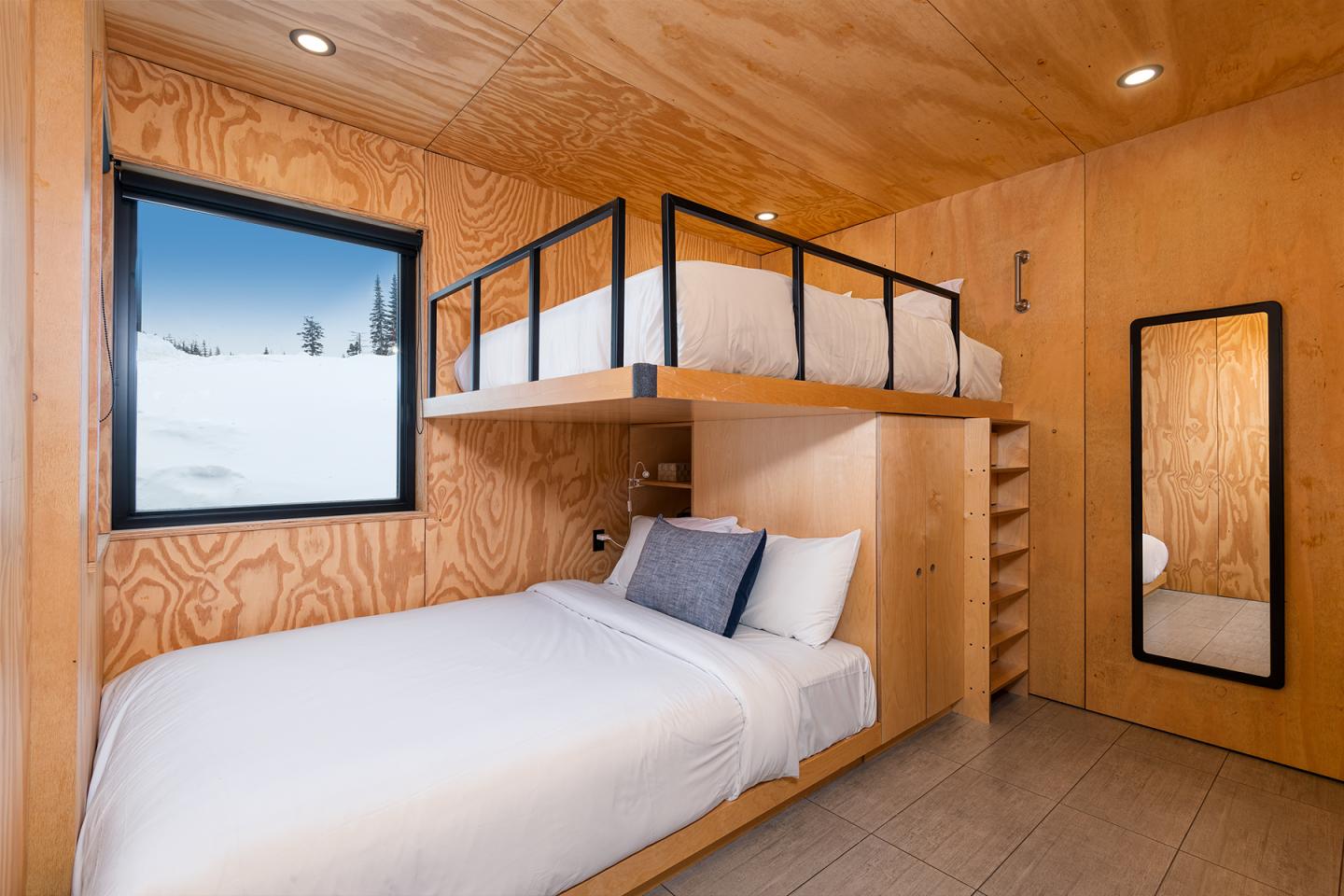 Chambre en bois avec deux lits superposés, fenêtre avec vue enneigée.