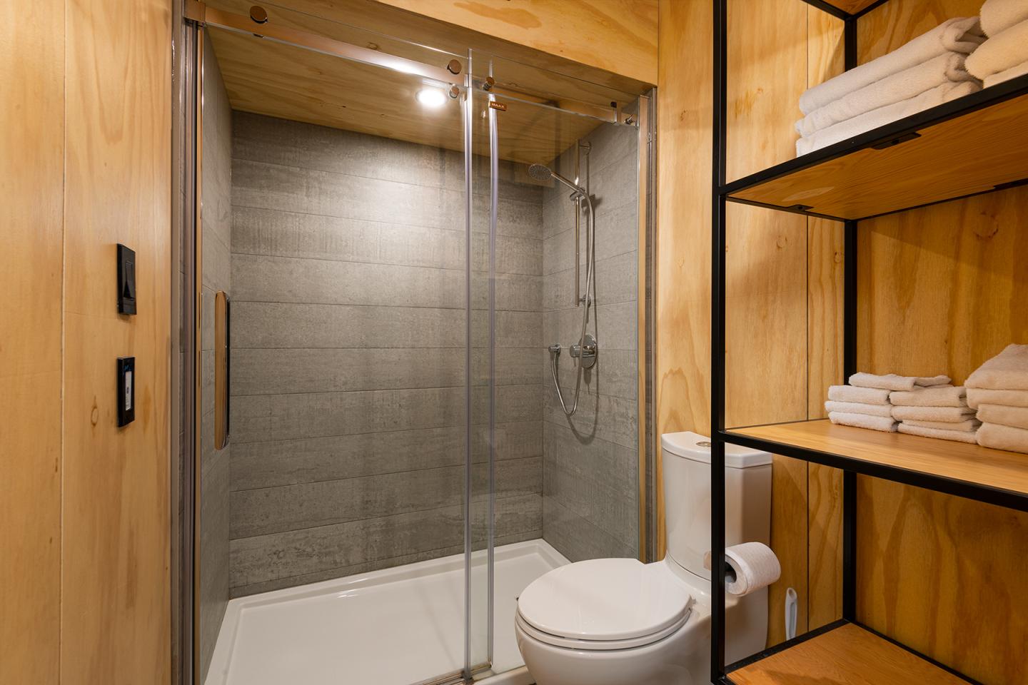 Salle de bain moderne en bois, douche vitrée, étagères avec serviettes.