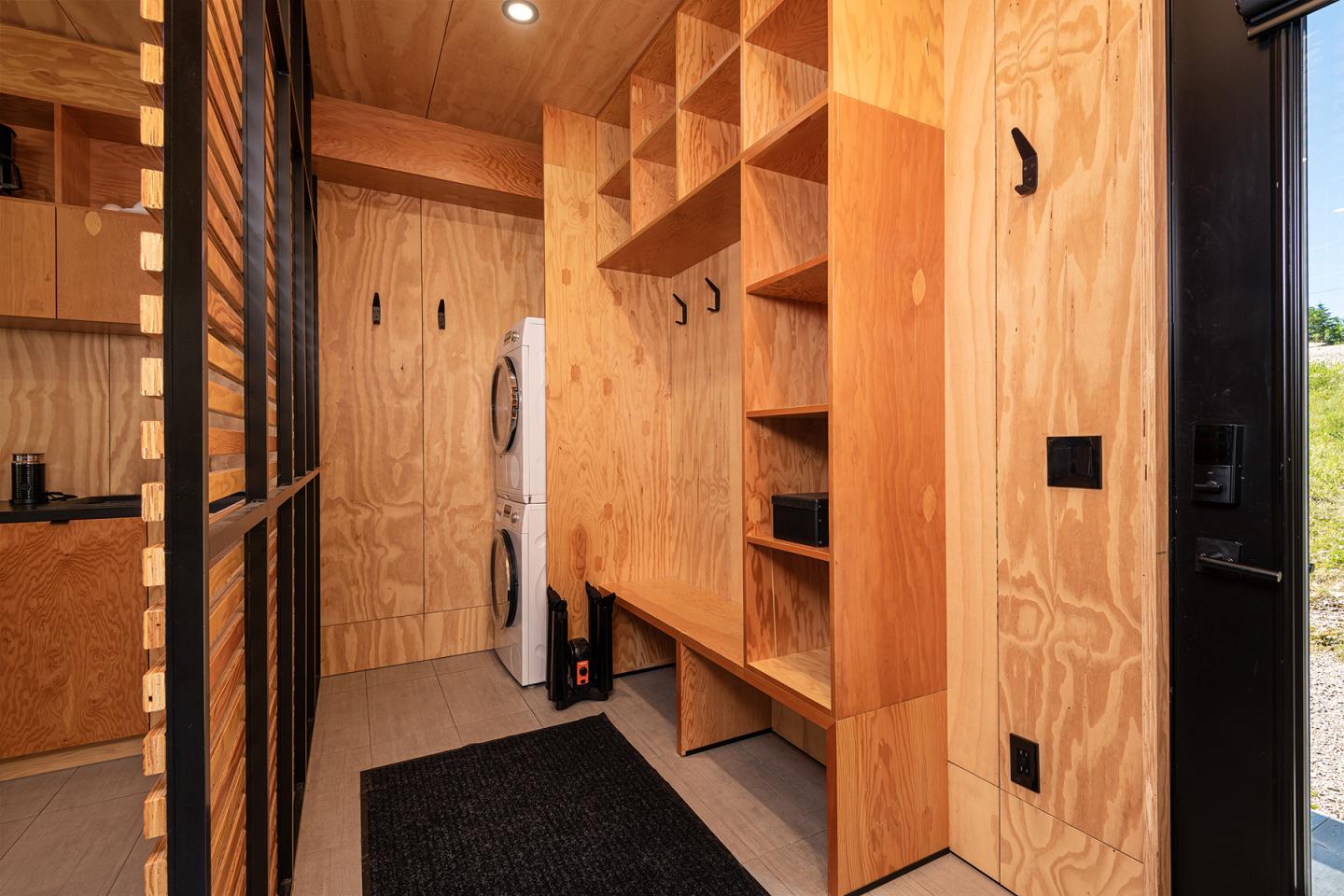 Couloir en bois clair avec étagères, sortie à droite, machine à laver blanche.