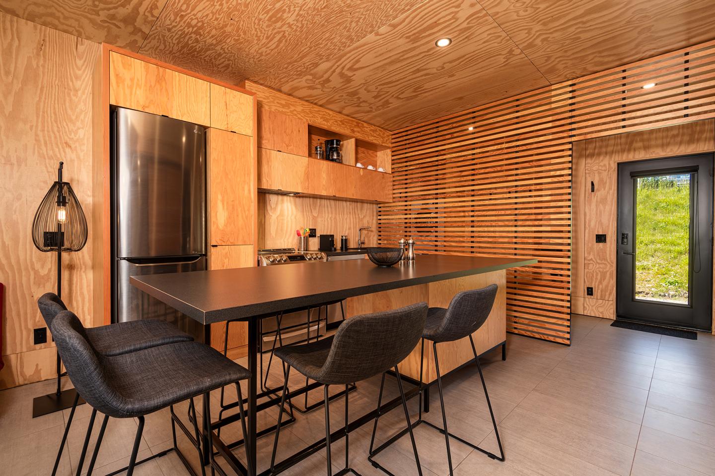 Cuisine moderne en bois, îlot central avec tabourets, éclairage chaleureux.