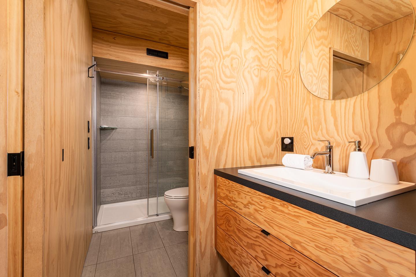 Salle de bain en bois clair avec douche moderne et lavabo sur meuble noir.