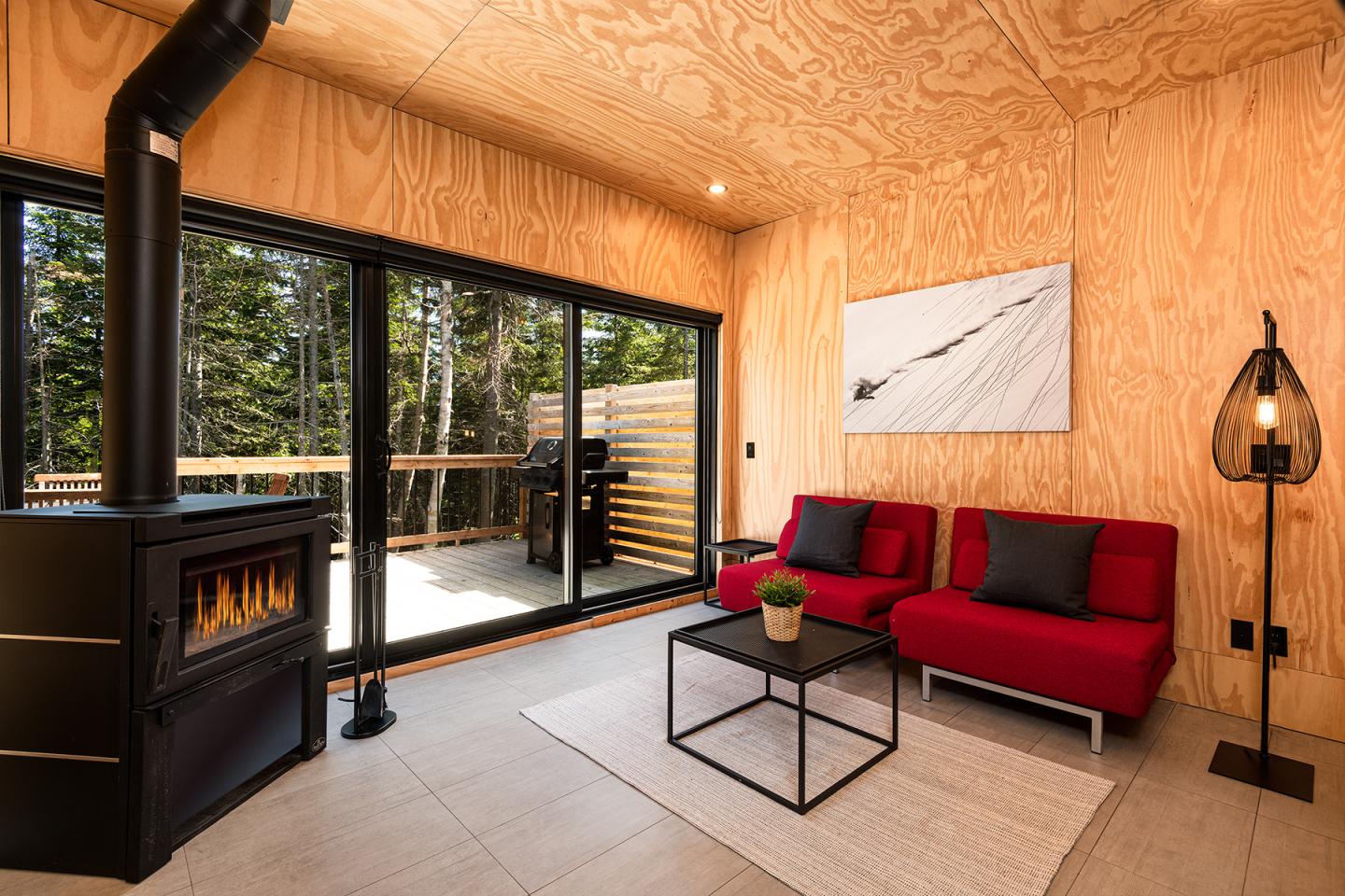 Salon moderne en bois avec canapé rouge, poêle noir, grande baie vitrée.