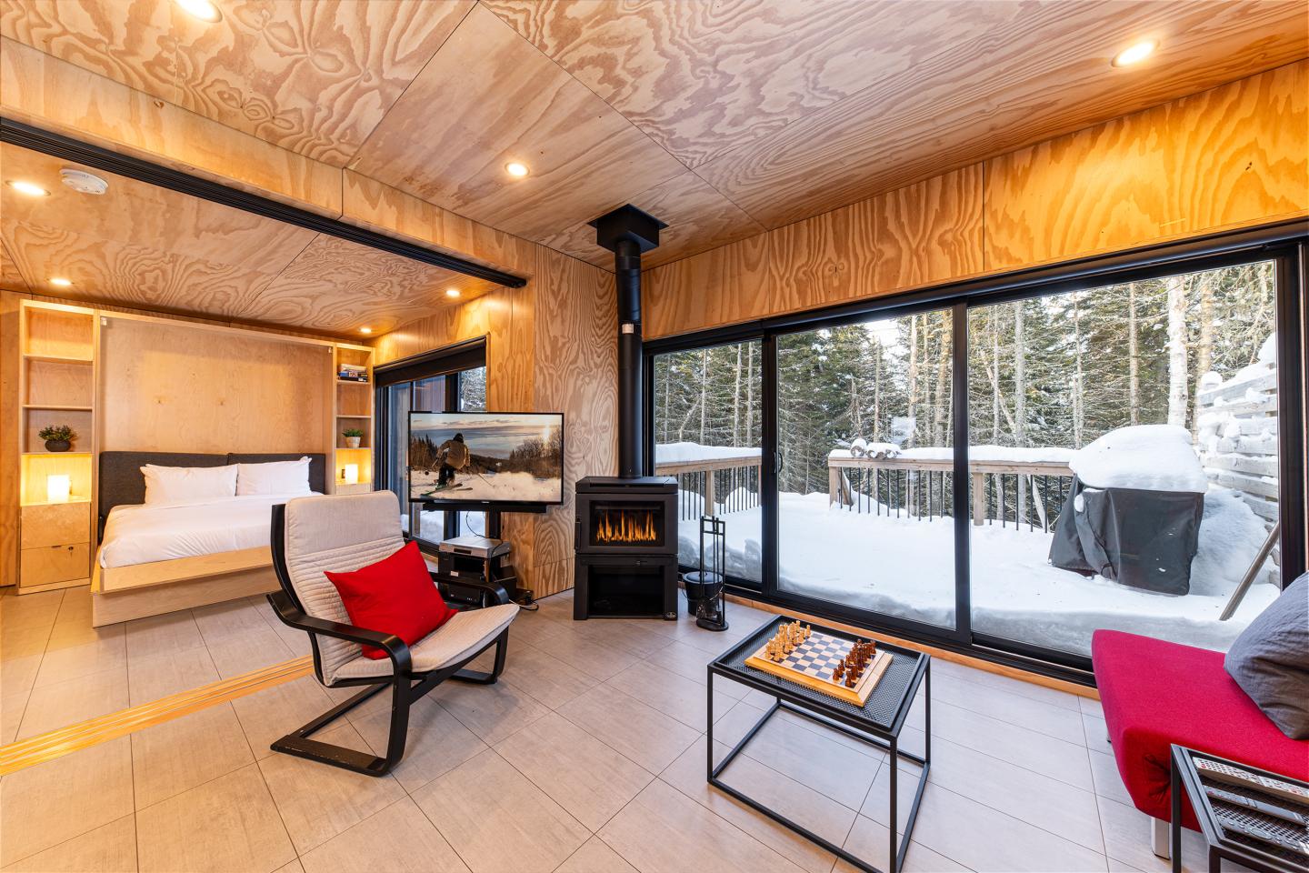 Salon moderne avec grande baie vitrée, vue sur neige et poêle à bois.