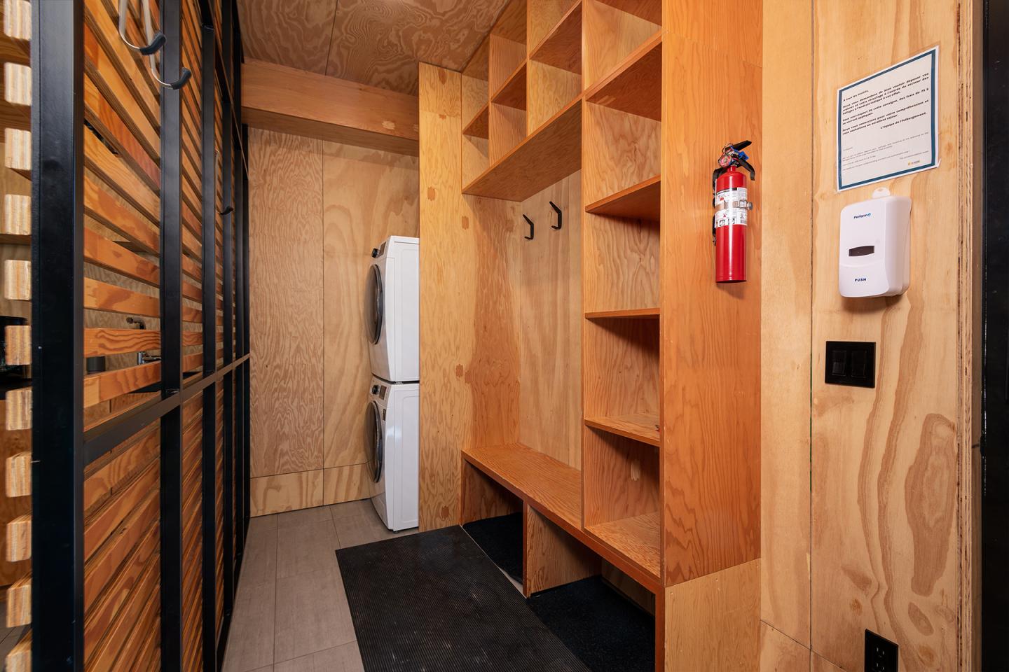 Couloir en bois avec casiers, réfrigérateur blanc et extincteur accroché.