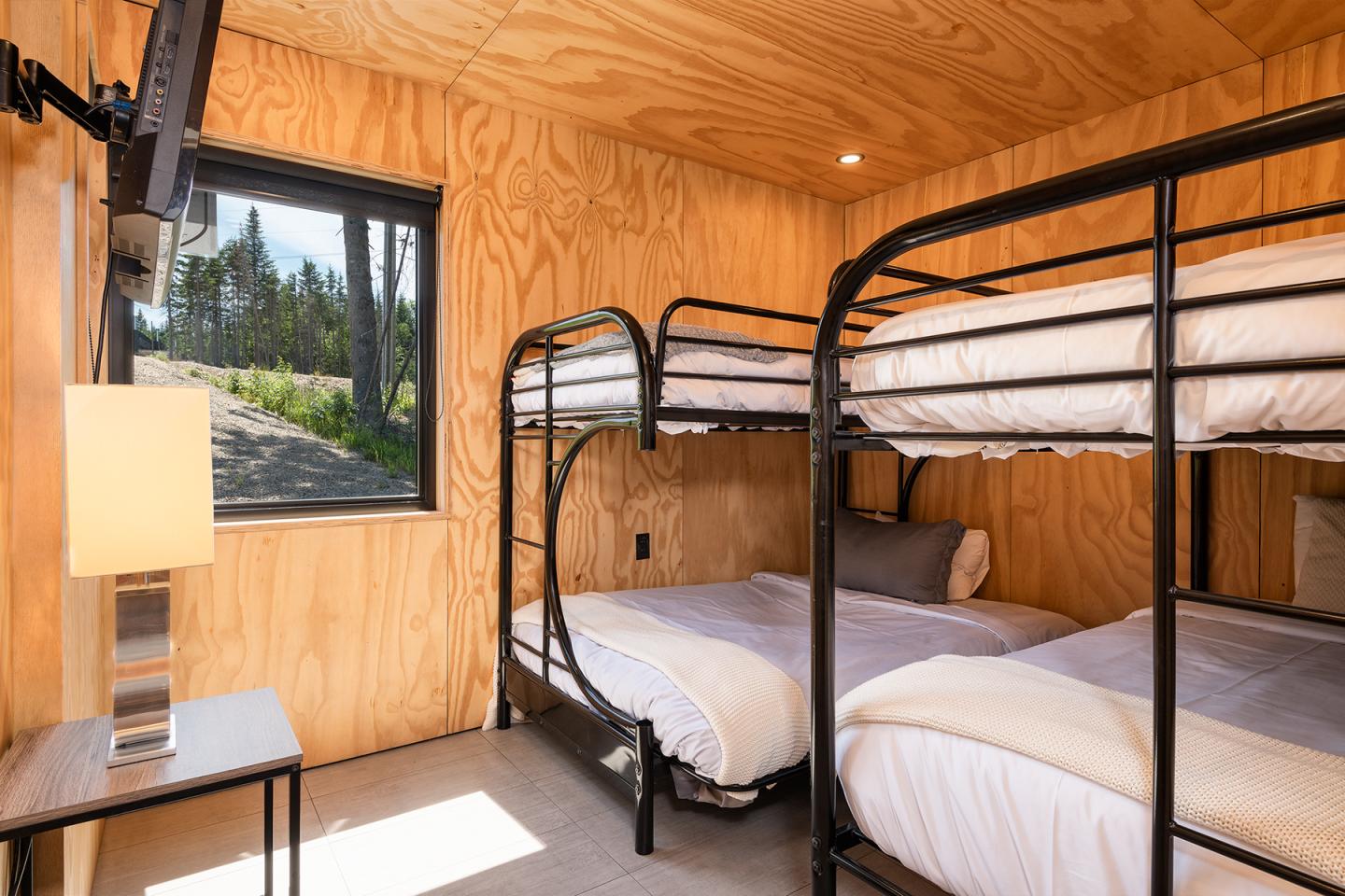 Chambre en bois avec lits superposés et fenêtre donnant sur une forêt.