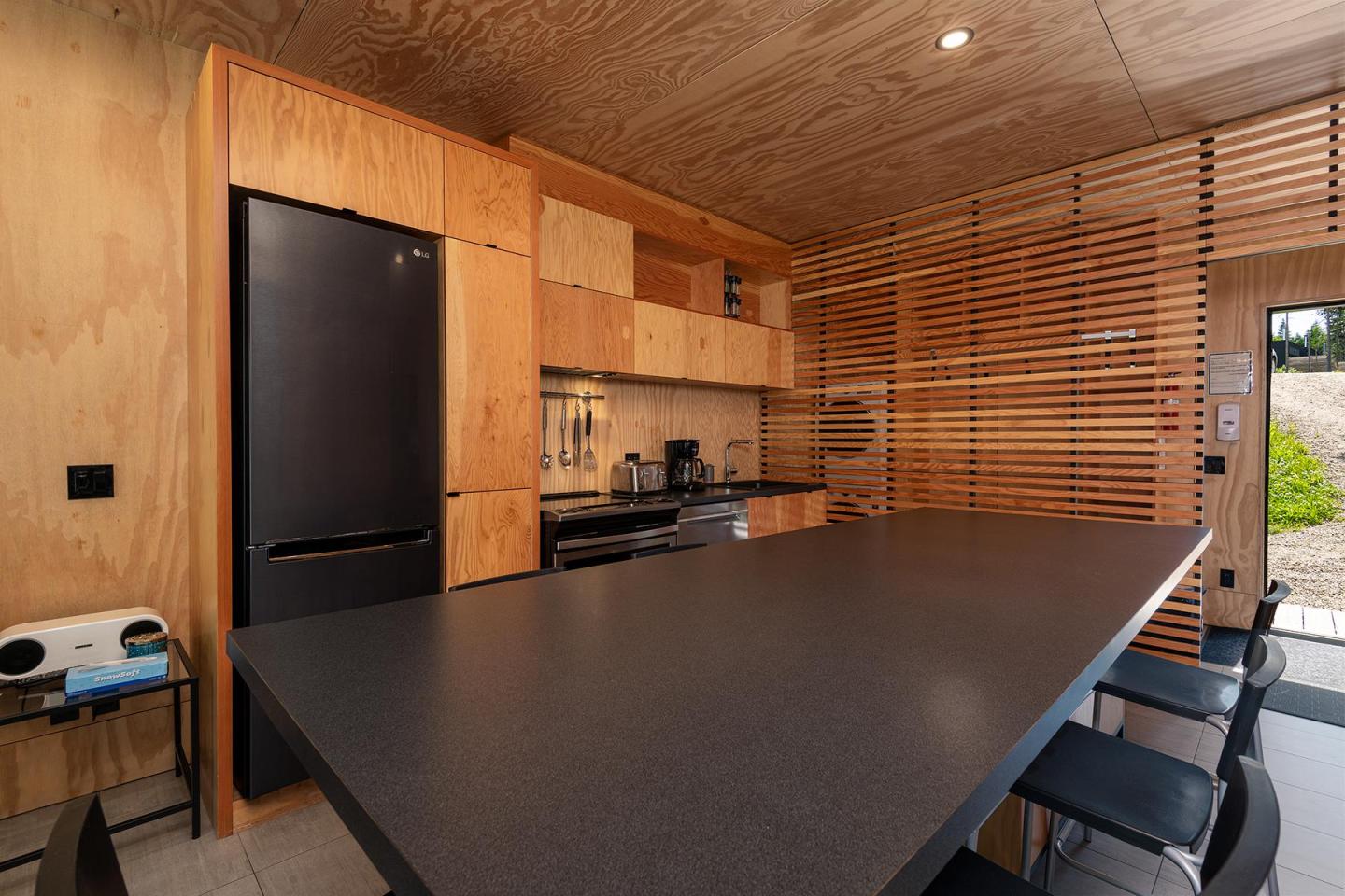 Cuisine moderne en bois avec frigo noir et table à manger, lumière naturelle.