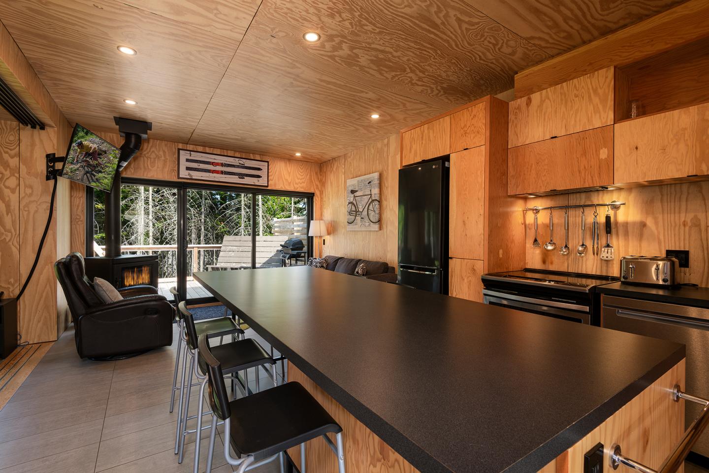 Cuisine moderne en bois clair avec un long comptoir noir et un coin salon avec fauteuils.