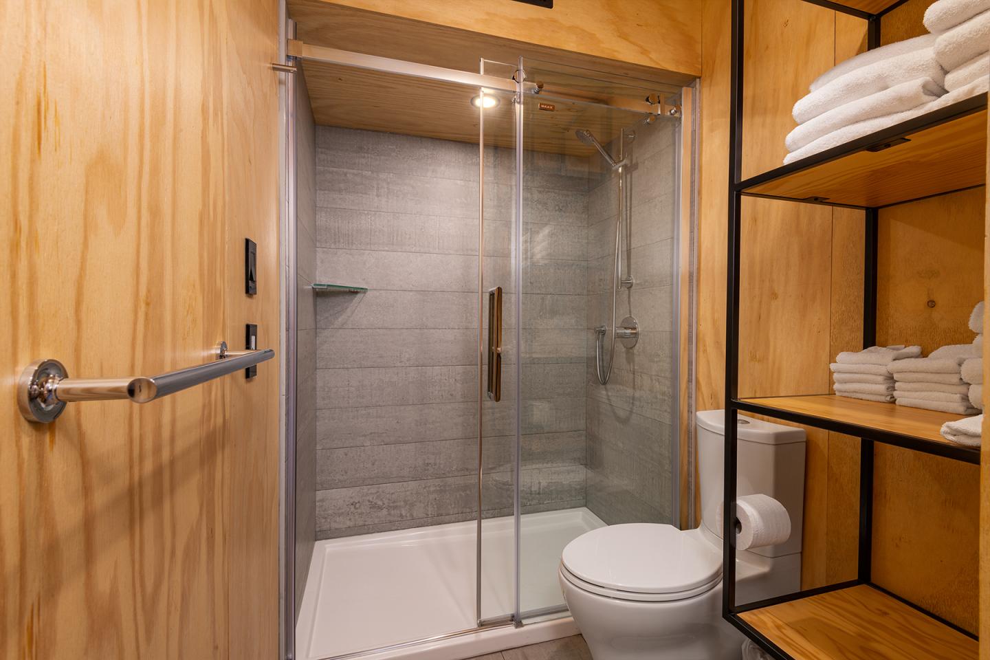Salle de bain moderne avec douche vitrée et étagères en bois.