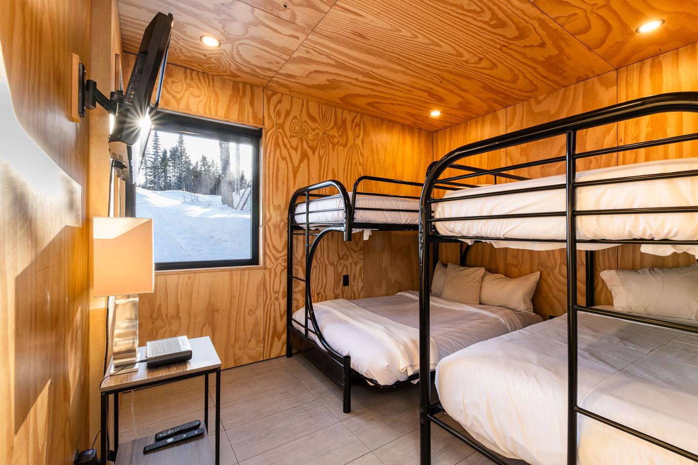 Chambre avec lits superposés, murs en bois, vue sur neige par la fenêtre.