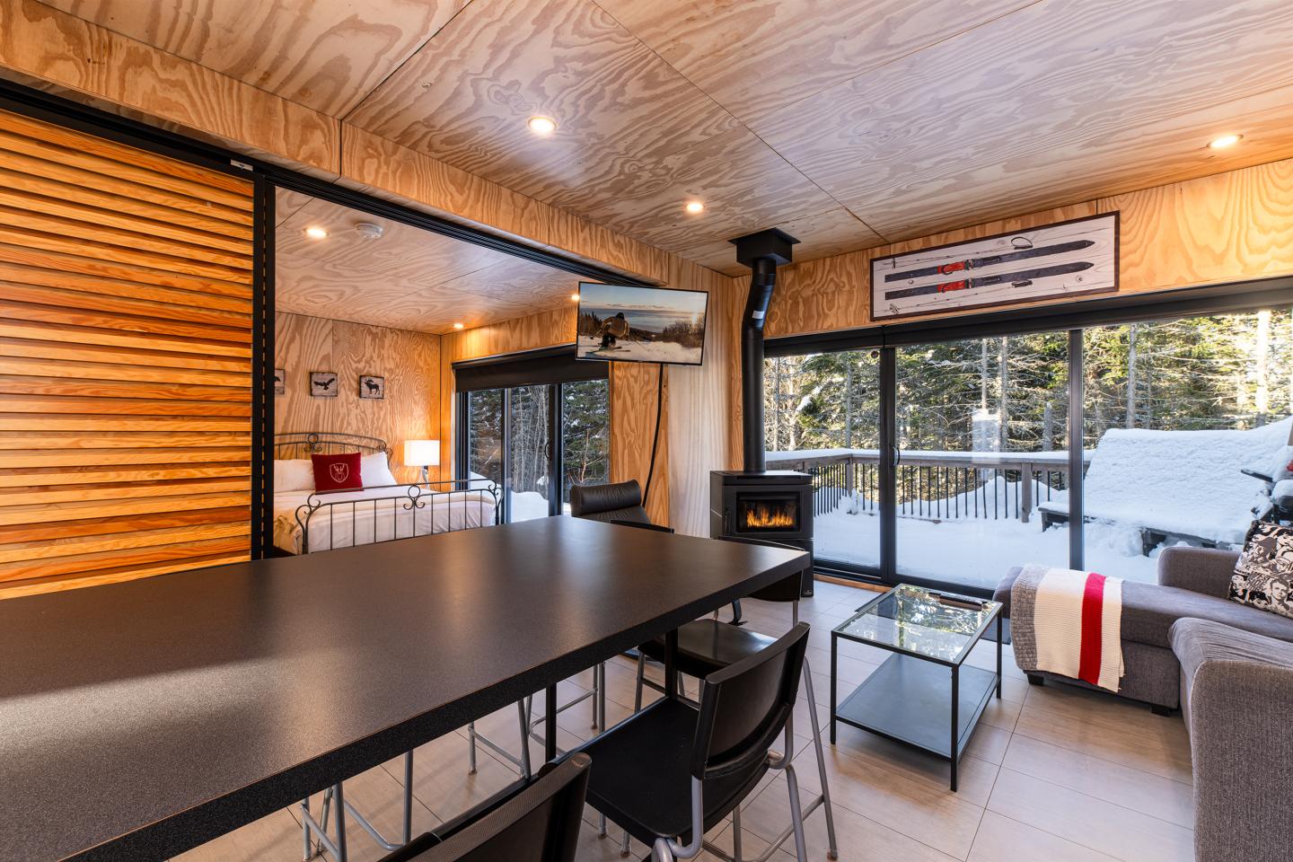 Intérieur de chalet moderne avec grandes fenêtres, cheminée et vue sur la neige.