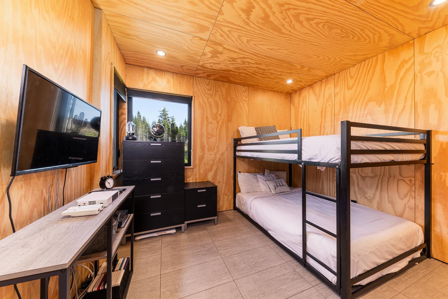 Chambre avec murs en bois, lits superposés, télé et commode noire.