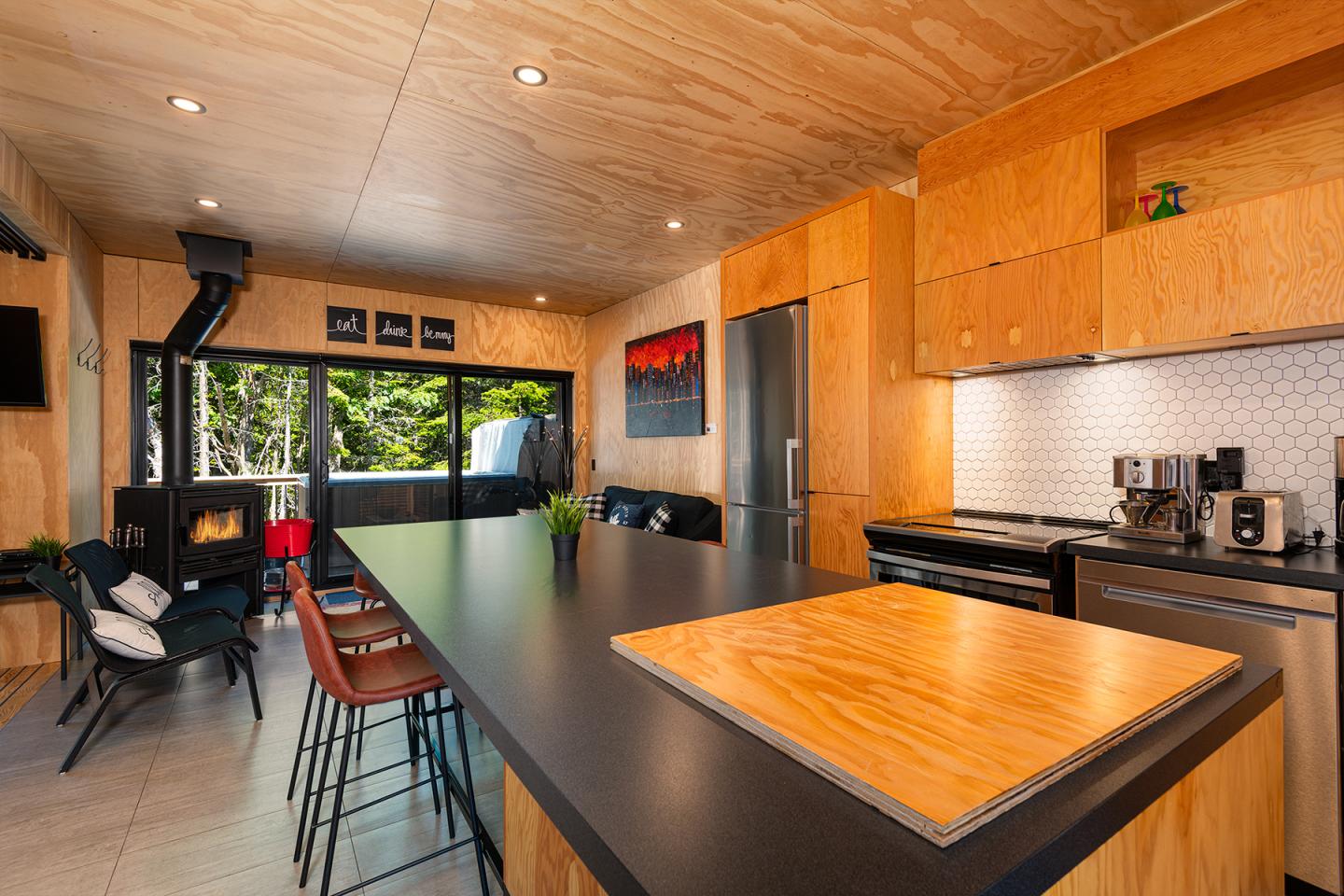 Cuisine moderne avec îlot en bois, poêle à bois et grandes fenêtres donnant sur la forêt.