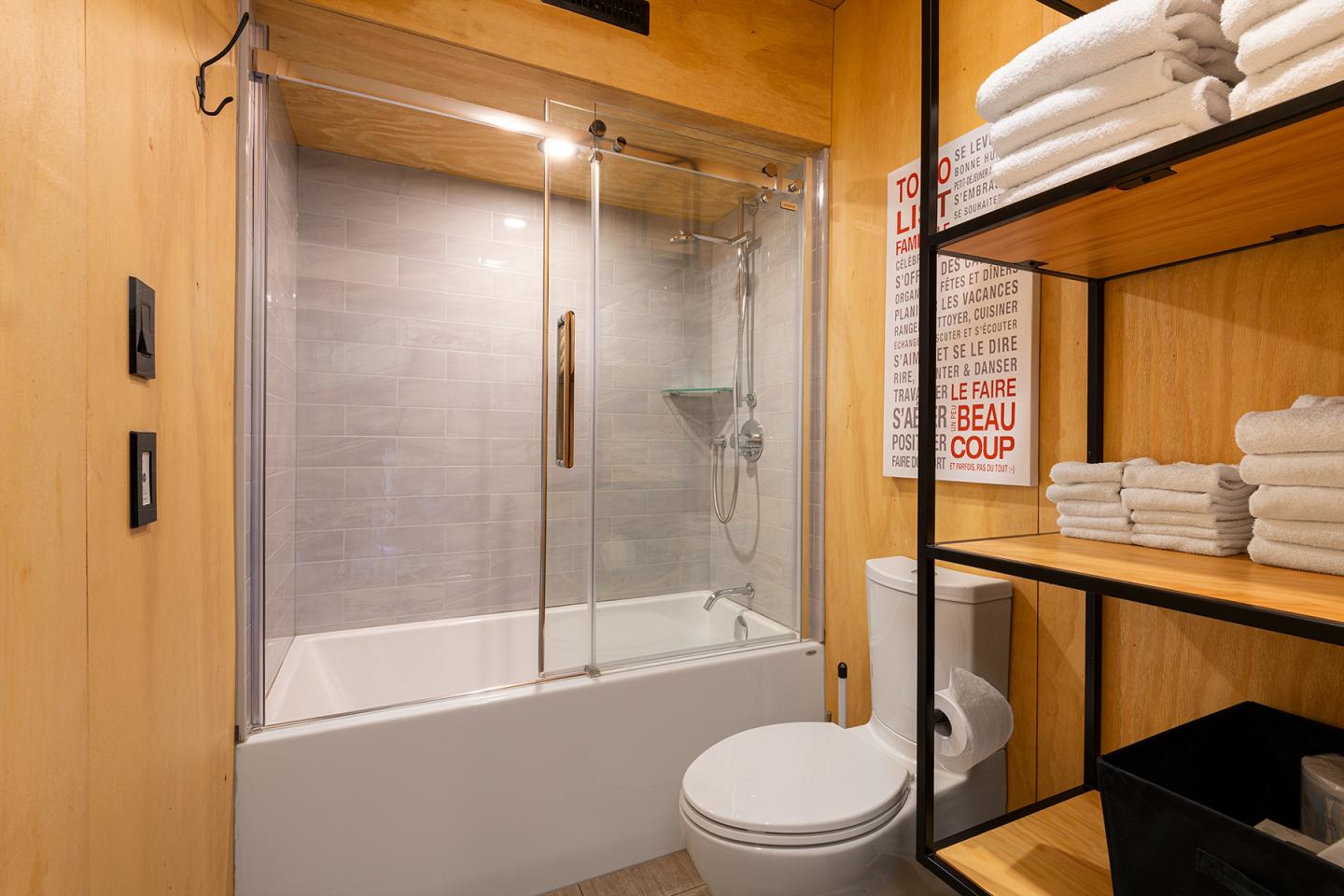 Salle de bain moderne avec baignoire, étagères et serviettes blanches.