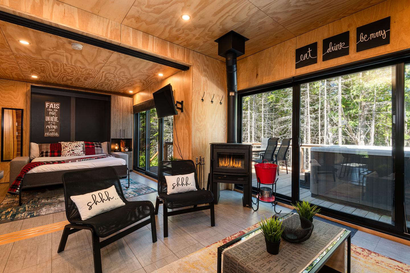 Salon moderne avec poêle à bois, grandes baies vitrées sur terrasse, et coin chambre.