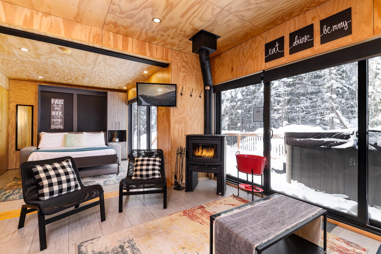 Chalet moderne avec poêle à bois, grande fenêtre et vue sur la neige.