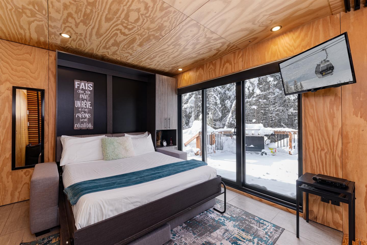 Chambre moderne avec baies vitrées, lit double et TV, vue sur la neige.
