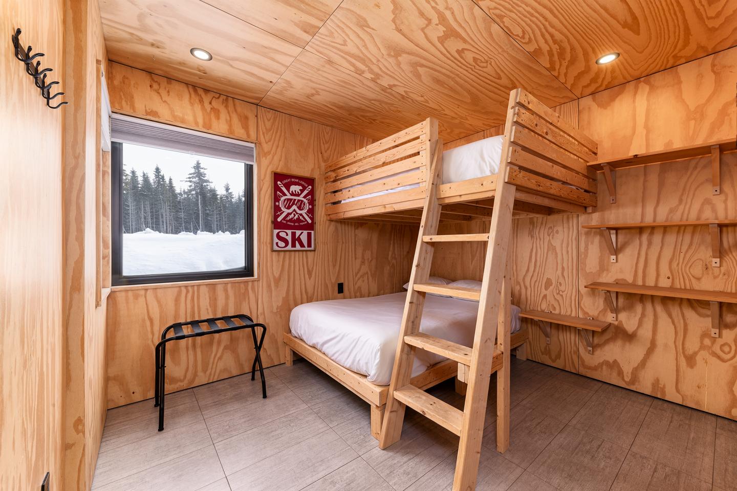 Chambre en bois avec lits superposés, vue neigeuse par la fenêtre.