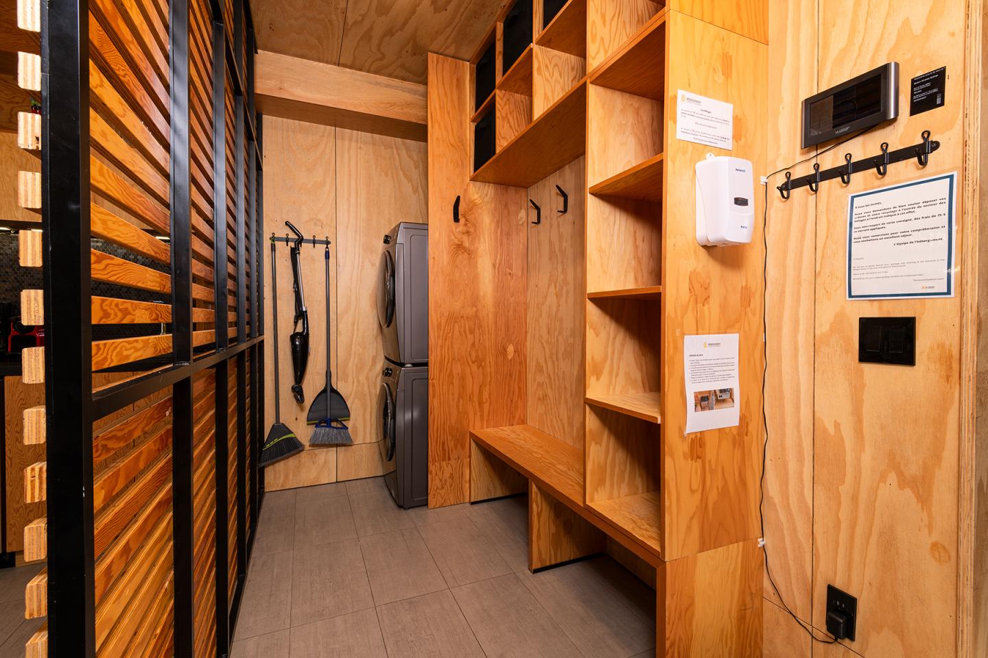 Vestiaire en bois avec étagères et banc, équipement de nettoyage accroché au mur.