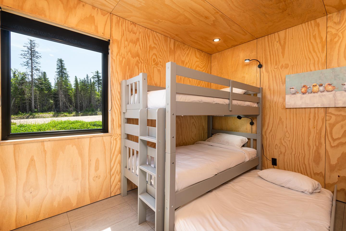 Chambre en bois avec lit superposé, fenêtre vue sur forêt.