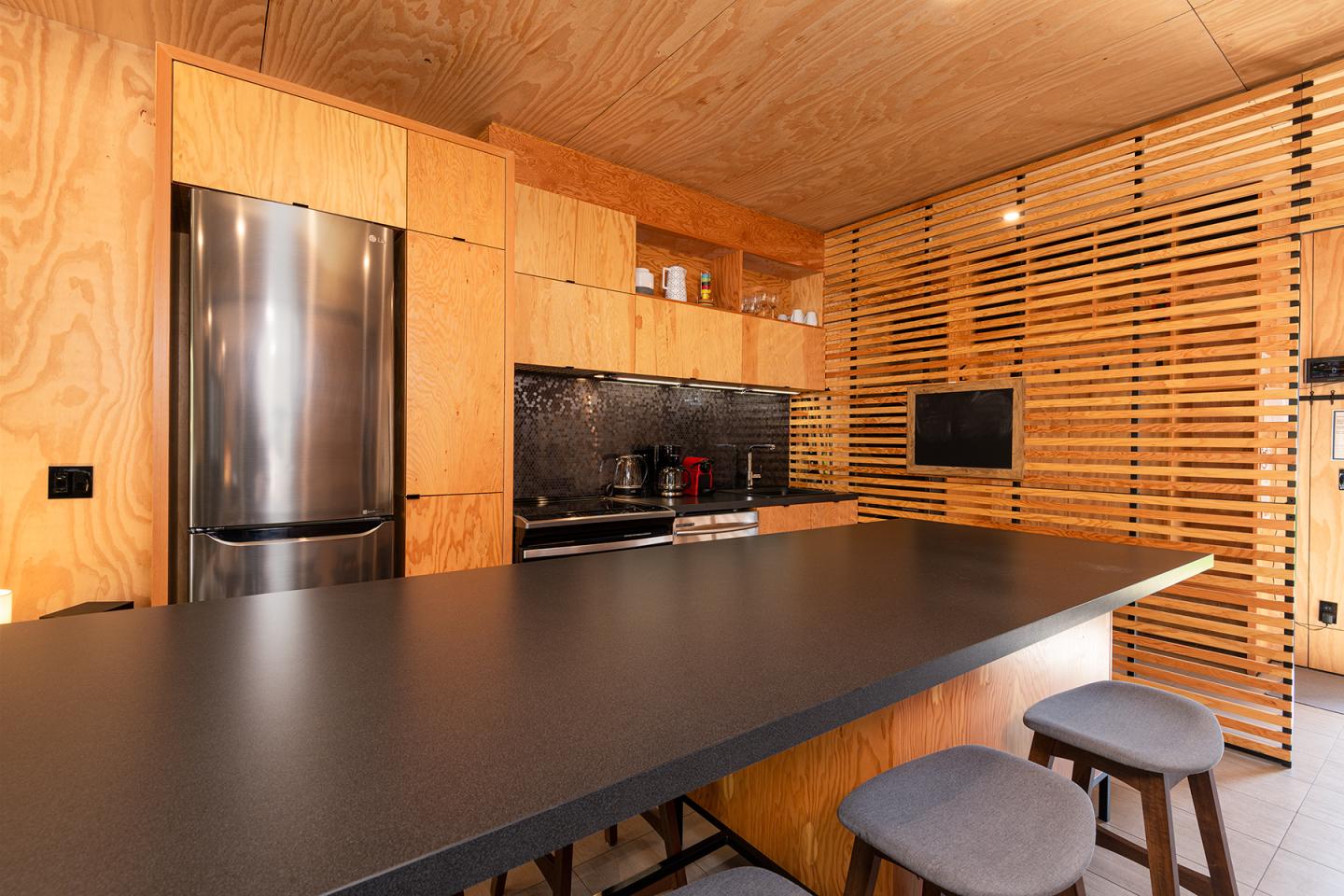 Cuisine moderne en bois, avec comptoir noir et tabourets gris.