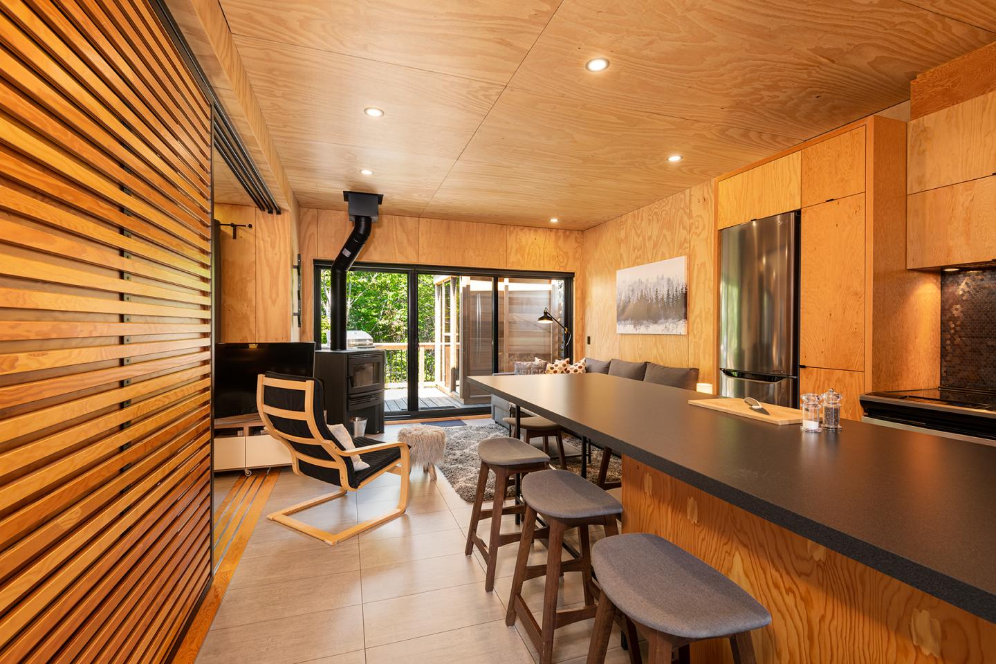 Intérieur moderne en bois, cuisine ouverte avec îlot et porte-fenêtre donnant sur l'extérieur.