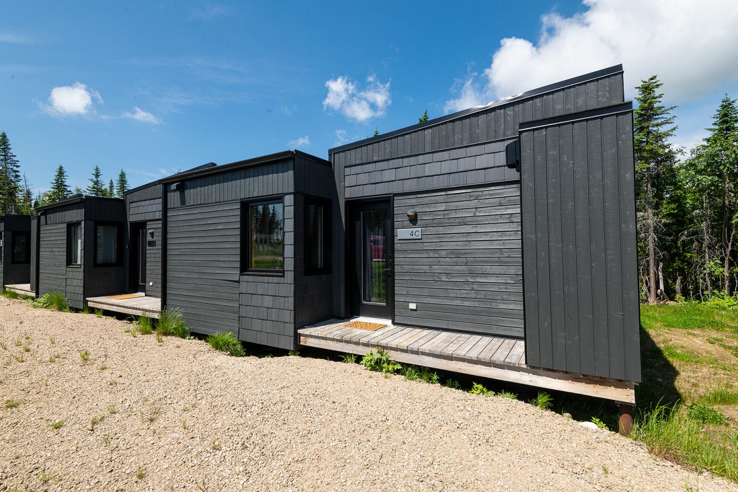 Petites maisons modernes noires alignées sur un chemin, ciel bleu en arrière-plan.