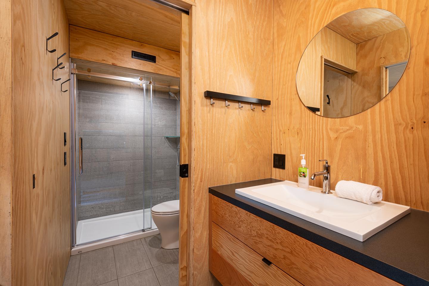 Salle de bain en bois, miroir rond, douche vitrée, lavabo moderne.